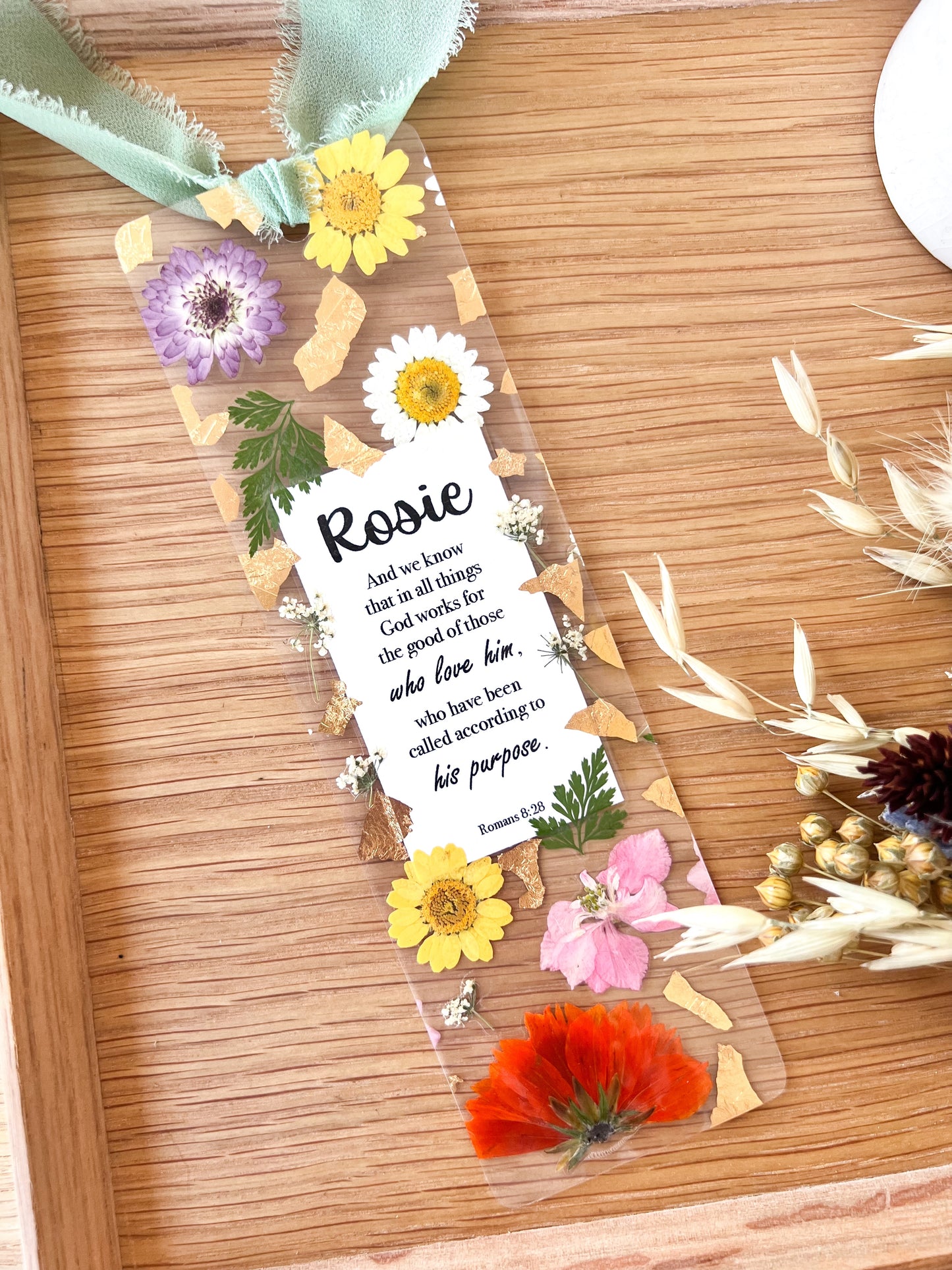 Bookmark includes the following scripture passage : "[custom name] And we know that in all things God works for the good of those who love him, who have been called according to his purpose. Romans 8:28"