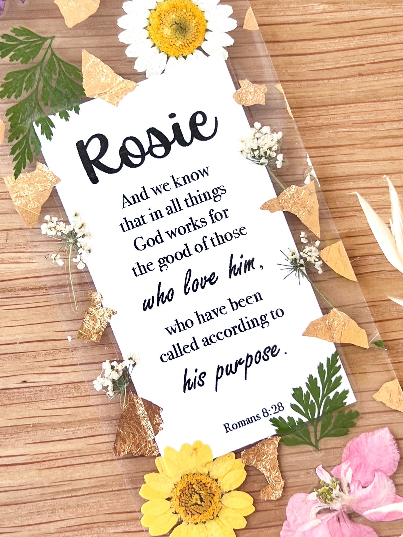 Bookmark includes the following scripture passage : "[custom name] And we know that in all things God works for the good of those who love him, who have been called according to his purpose. Romans 8:28"